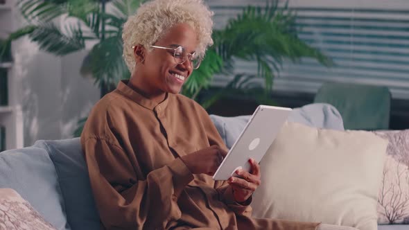 African Woman on Sofa with Digital Tablet in Hands Enjoying Social Networks