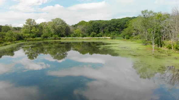 left drone flight over small lake covered in algae nest to rural road 4k