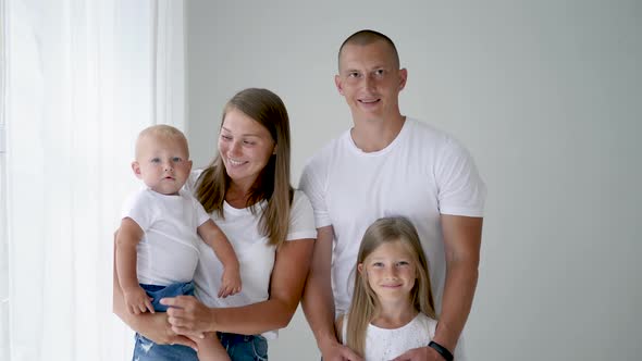 Family of Four Stands in a White Room Against