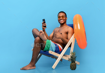 hair with cellphone, recommending new mobile app, showing thumb up on blue studio background. Cheerful young guy shopping online. Summer sale