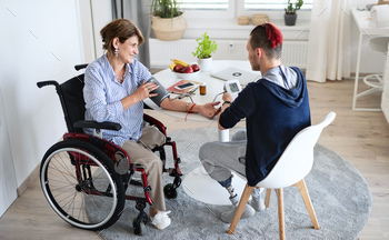 Disabled people in wheelchair sitting at the table indoors at home, measuring blood pressure / Photodune, Misc