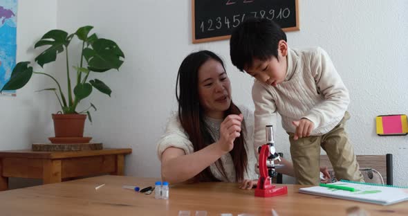 Asian mother and little boy looking at a microscope at home