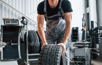 Rolls the tire. Adult man in grey colored uniform works in the automobile salon / Photodune, Misc