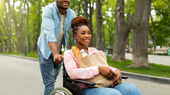 Millennial black handicapped woman in wheelchair holding paper bag with food, going shopping with / Photodune, Misc