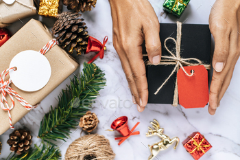 A hand holding a black gift box on a white cement floor / Photodune, Misc