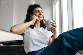 Smiling brunette woman talking on mobile phone while drinking coffee / Photodune, Misc