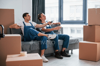 Tired and taking break. Two young movers in blue uniform working indoors in the room / Photodune, Misc