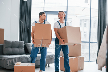 Busy day. Two young movers in blue uniform working indoors in the room / Photodune, Misc