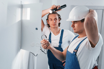 Two young male electricians works indoors together. Using flashlight / Photodune, Misc