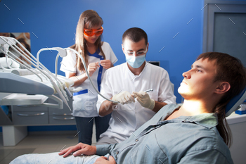 Young dentist doctor man in white uniform and special mask and young nurse woman examining man / Photodune, Misc