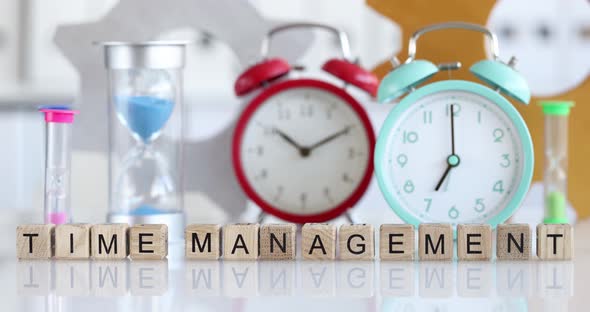 Many Alarm Clocks and Hourglasses Standing on Table Near Wooden Cubes Closeup  Movie