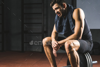 Tired young sportsman with towel on neck sitting on barbell in gym / Photodune, Misc