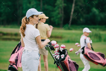 selective focus of women in caps with golf gear walking on green lawn at golf course / Photodune, Misc