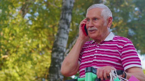 Elderly Old Grandfather Man on Electric Scooter with Colorful Shopping Bags Talking on Mobile Phone