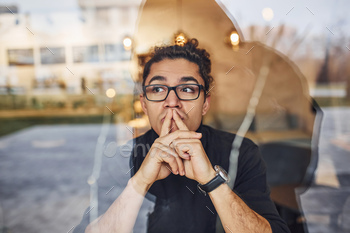 Young guy with black curly hair sitting indoors in cafe. View through the glass / Photodune, Misc