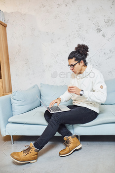 Handsome young man with curly black hair and cup of drink indoors with laptop / Photodune, Misc