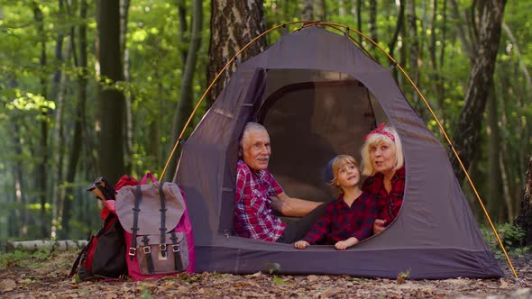 Senior Grandmother Grandfather with Granddaughter Sitting in Tourist Tent Over Campfire in Wood