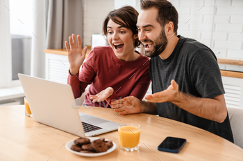 Happy young couple smiling and using laptop while sitting at home / Photodune, Misc