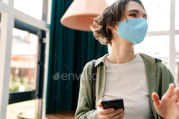 Happy girl in protective mask using cellphone while standing / Photodune, Misc