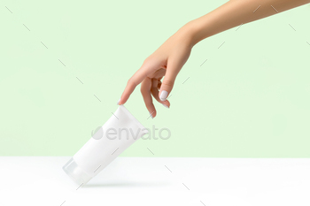 Womans hand holding white tube on pastel green background / Photodune, Misc
