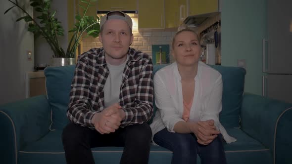 A Guy and a Girl Watching TV Sitting on the Couch at Home in the Background of the Kitchen