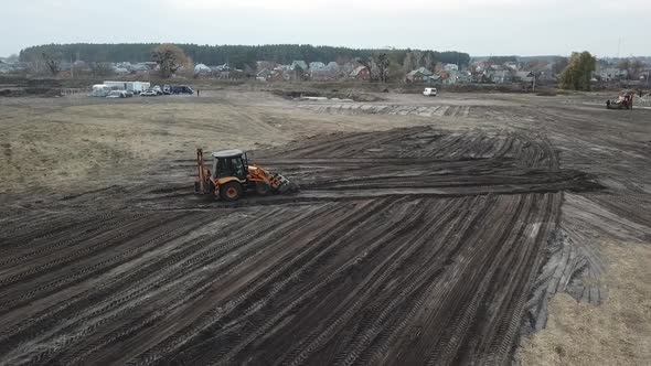 Drone is Flying Over the Dirt Field with an Excavator Leveling the Ground