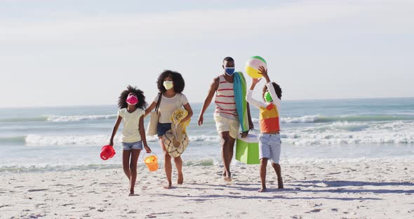 African american parents and their children wearing face masks carrying beach equipment on the beach