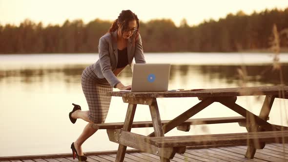 Serious Business Woman in Glasses Bends Over and Uses Laptop Outdoors During Quarantine
