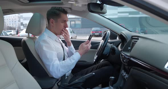 Shocked Businessman Scared By a Bad Message on His Smartphone Sitting in the Driver's Seat in the