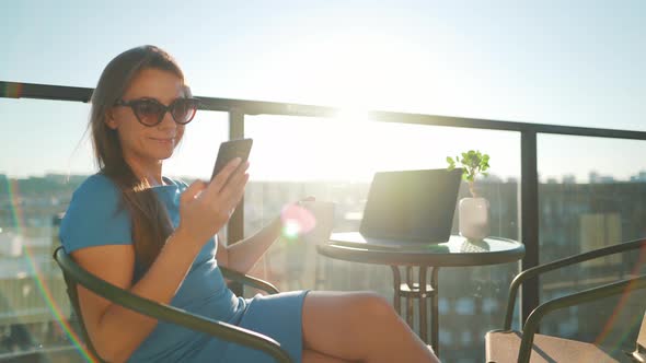 Woman Using Smartphone on the Balcony Against the Backdrop of the Sunset. Outdoor Home Office