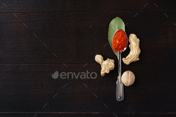 Spoon of chili powder surrounded with bay leaf, ginger and nutmeg on black wooden surface / Photodune, Misc