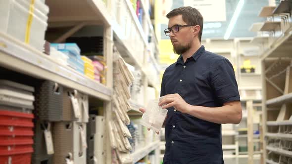 Householder is Comparing Two Plastic Boxes in Supermarket Standing Near Shelves