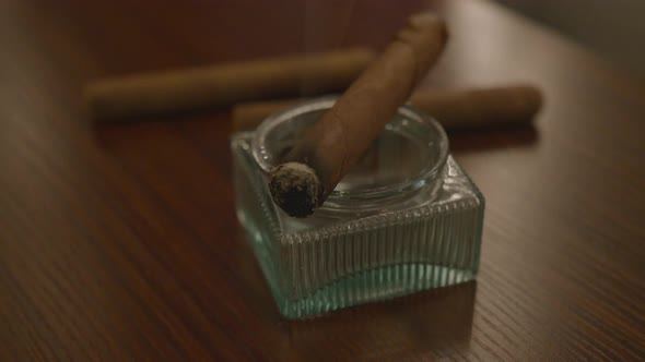 Close Up Pan of a Lit Cigar and an Ashtray on a Table