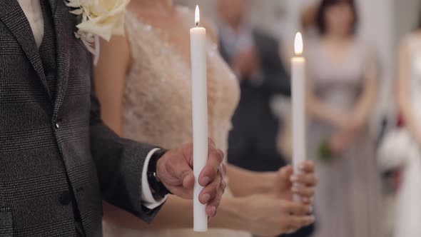 Newlyweds Bride and Groom Stand and Pray in Church Holding Candles in Hands Wedding Ceremony