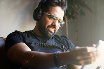Young happy bearded man sitting home and using digital tablet for surfing web internet. / Photodune, Misc