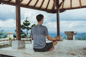 Young fashionable man meditating in the gazebo on the background of the mountains in Bali / Photodune, Misc