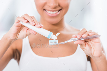 partial view of young woman putting toothpaste on toothbrush / Photodune, Misc