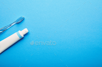 top view of toothbrush and toothpaste arranged on blue backdrop, dentistry concept / Photodune, Misc