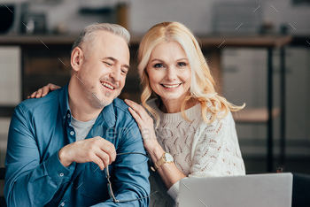 handsome man holding glasses and smiling with cheerful wife while looking at laptop / Photodune, Misc