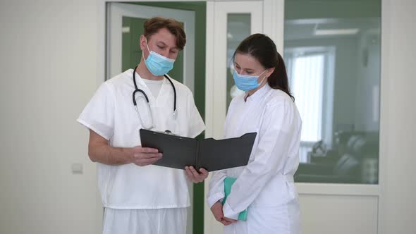 Concentrated Man and Woman Discussing Medical History Standing in Hospital Corridor