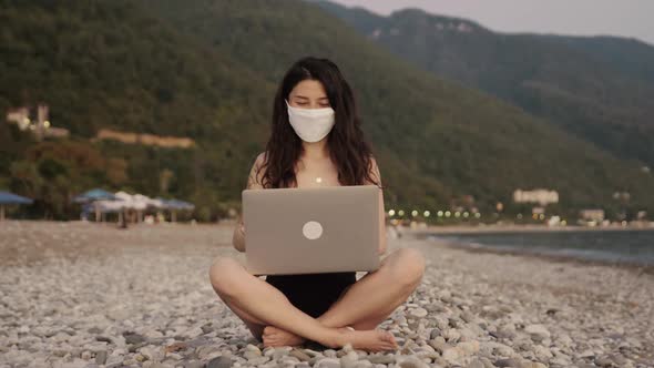 Pretty Businesswoman in Bikini in Medical Mask Working on Laptop Alone By the Sea at the Beach