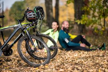 Close-up view of two mountain bikes with helmets and couple of cyclists sitting in autumn park / Photodune, Misc