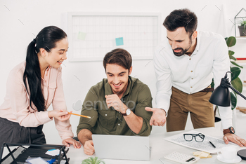 smiling managers sitting at desk and pointing at laptop screen in office / Photodune, Misc