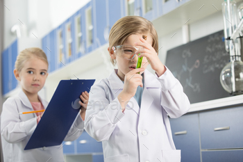 Preteen schoolboy in lab coat looking at sample in test tube / Photodune, Misc