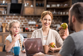 Happy young family in kitchen using laptop and eating fresh apples / Photodune, Misc