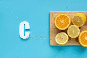 top view of ripe cut lemon and orange on wooden cutting board near letter C on blue background / Photodune, Misc