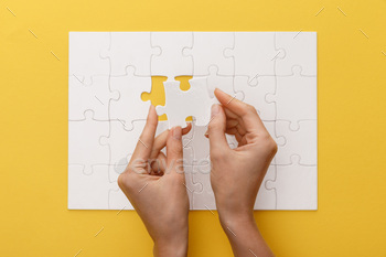 cropped view of woman holding piece of white jigsaw puzzle on yellow background / Photodune, Misc