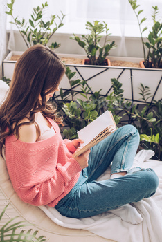 young woman reading book while sitting surrounded by green plants at home / Photodune, Misc