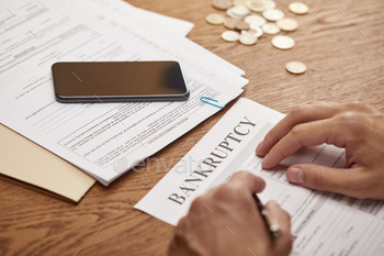 partial view of businessman filling in bankruptcy form at wooden table with smartphone and coins / Photodune, Misc