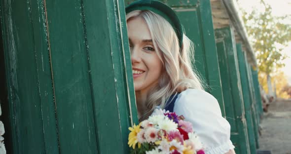 Girl with Bouquet of Flowers Looks Out of the Stable Door and Flirts with Camera